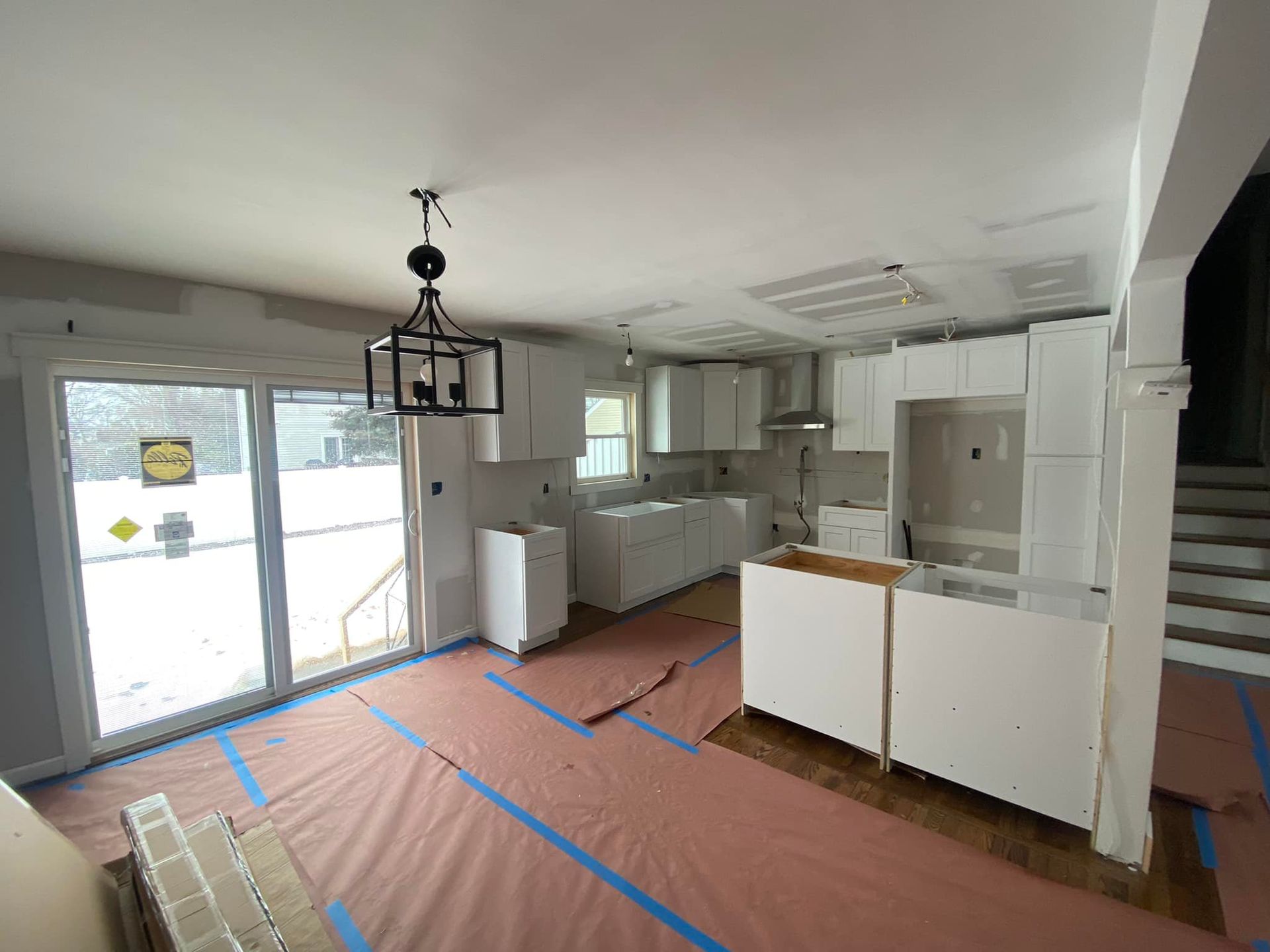 A kitchen under construction with white cabinets and a chandelier hanging from the ceiling.