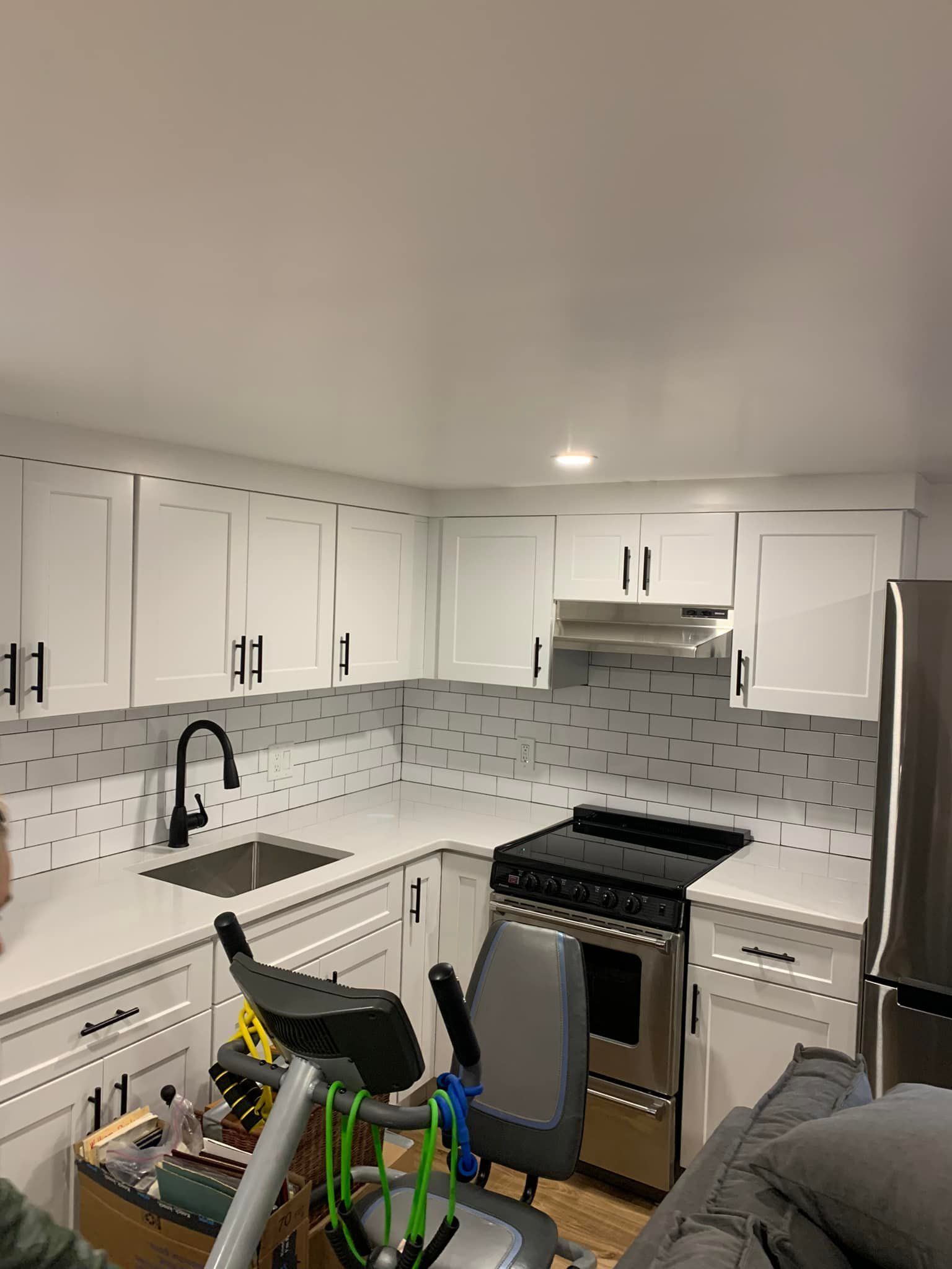 A kitchen with white cabinets , a stove , a sink , and a chair.