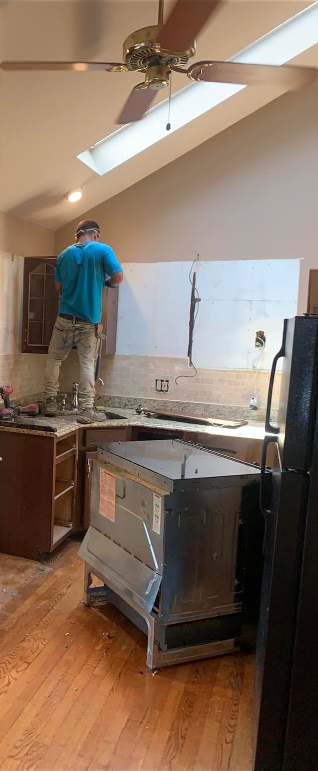 A man is standing in a kitchen with a ceiling fan.