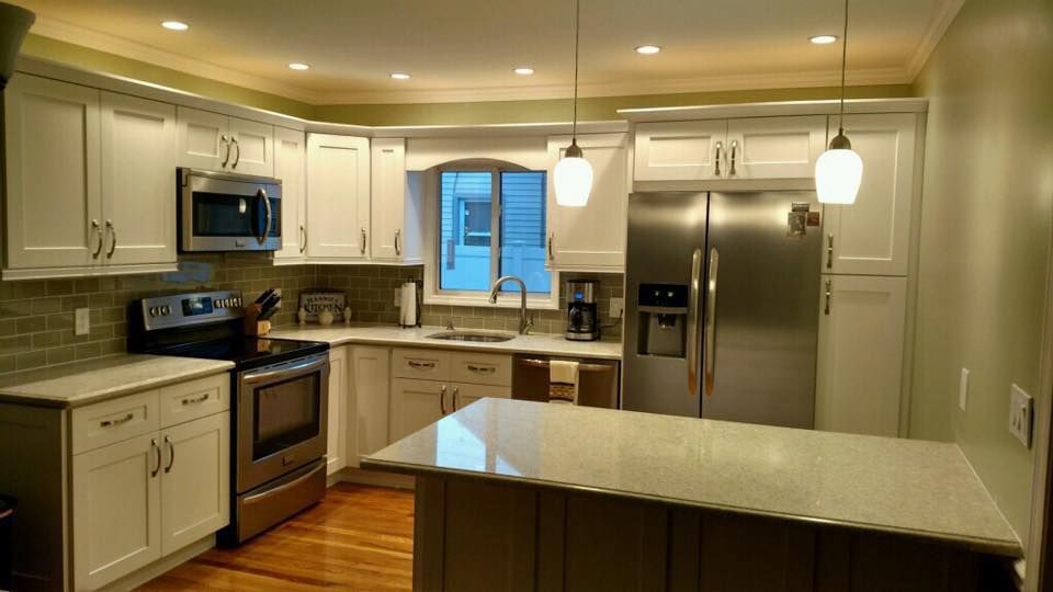A kitchen with white cabinets , stainless steel appliances , and a large island.