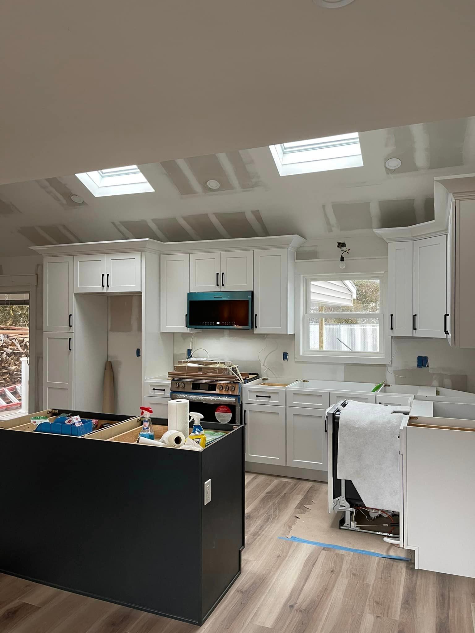 A kitchen under construction with white cabinets and a black island.