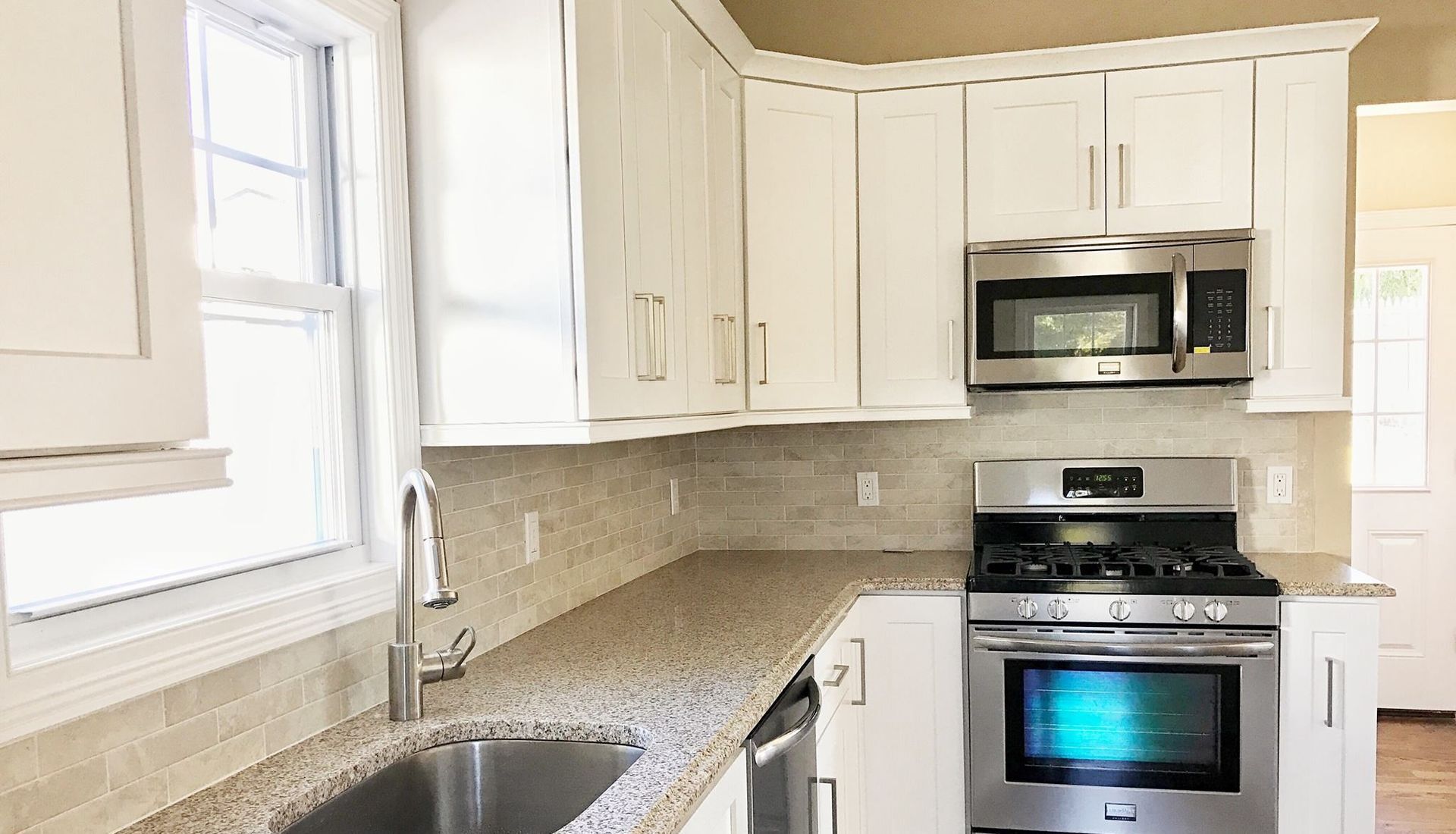 A kitchen with granite counter tops , stainless steel appliances , and white cabinets.