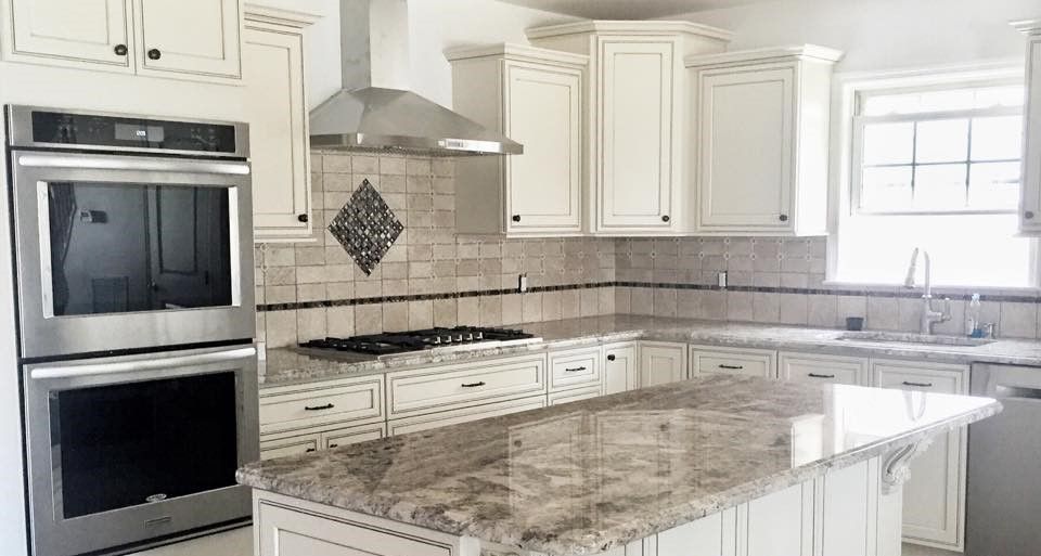 A kitchen with white cabinets , granite counter tops , stainless steel appliances and a large island.