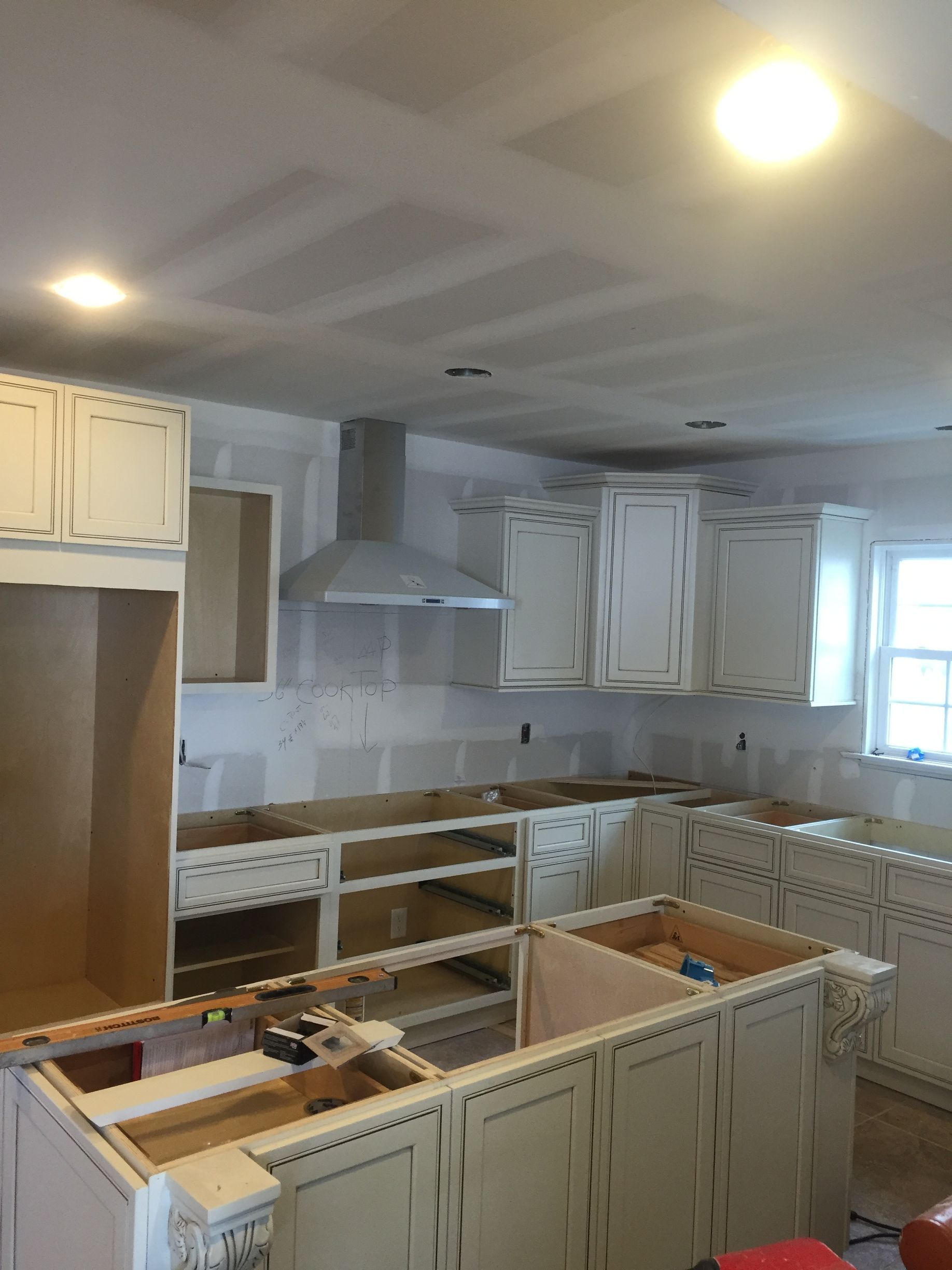 A kitchen under construction with white cabinets and a hood.