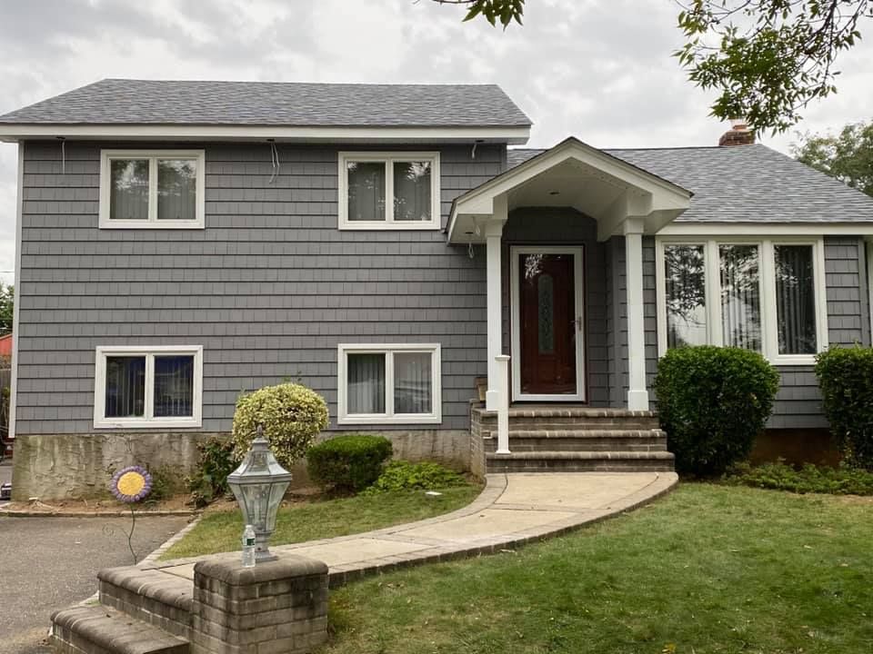 A gray house with white trim and a red door is sitting on top of a lush green lawn.