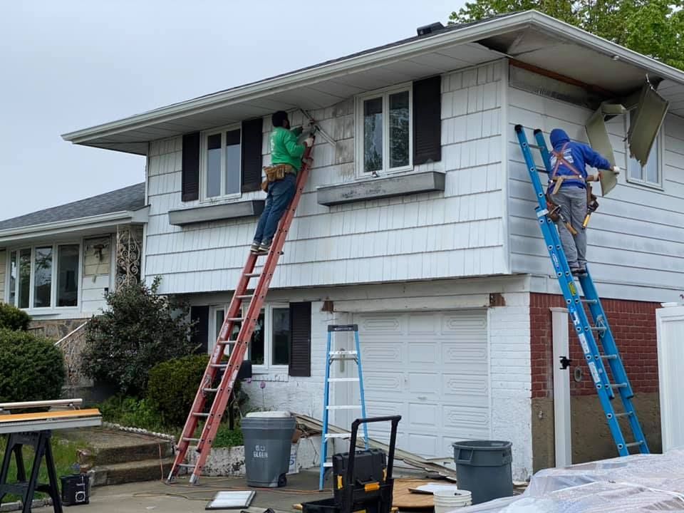 Two men are painting the side of a white house.