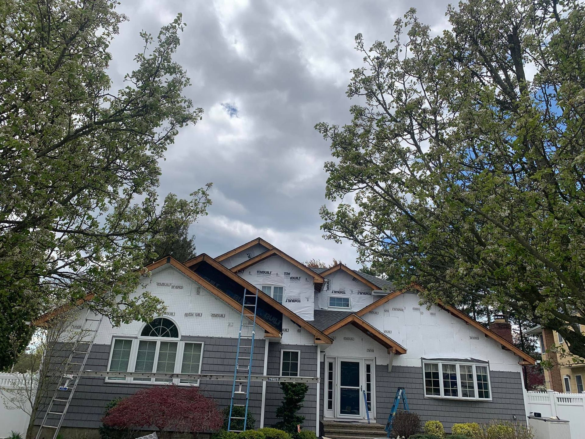 A large house is being remodeled with a ladder in front of it.