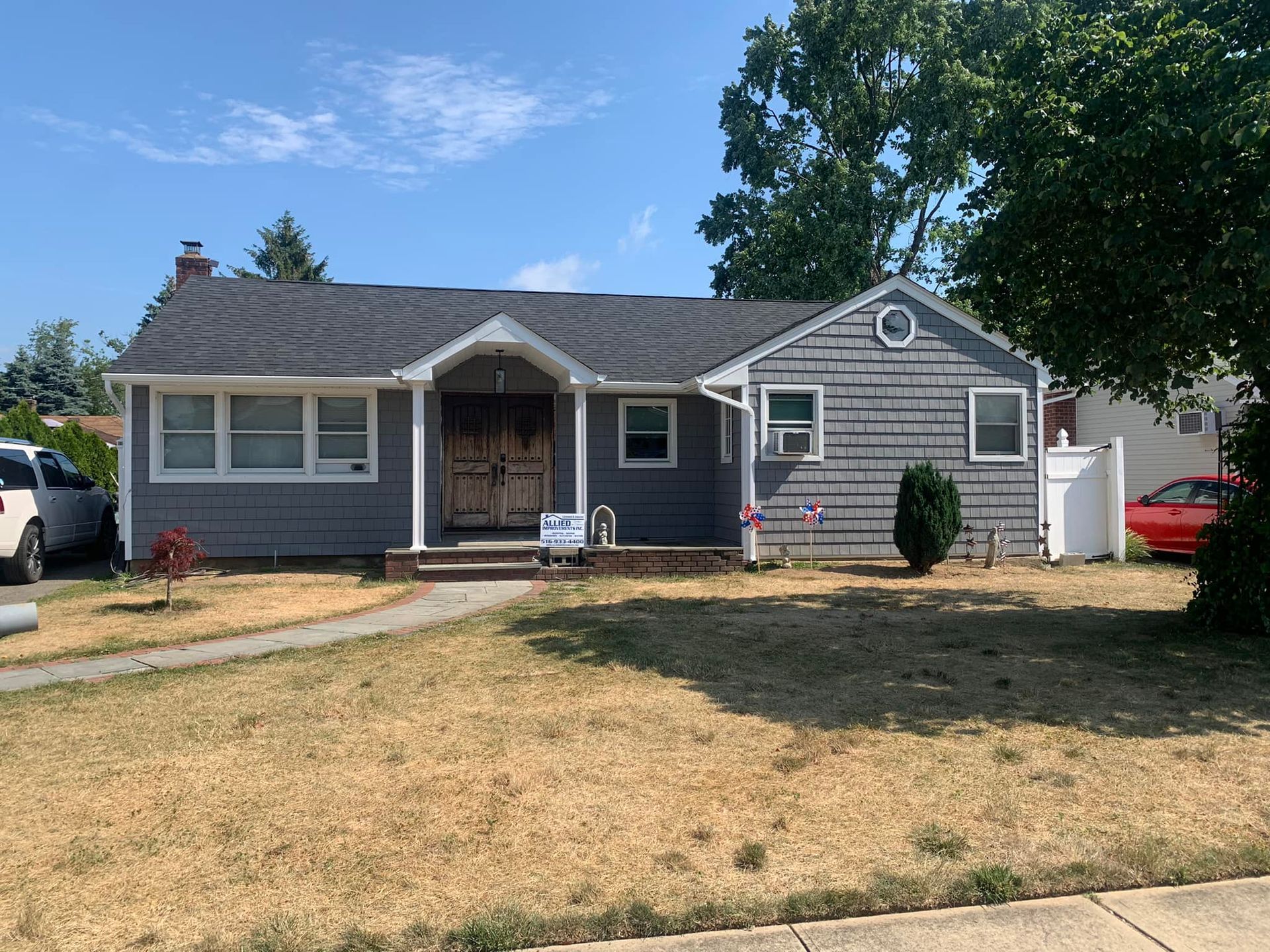 A gray house with a gray roof and a red car parked in front of it.