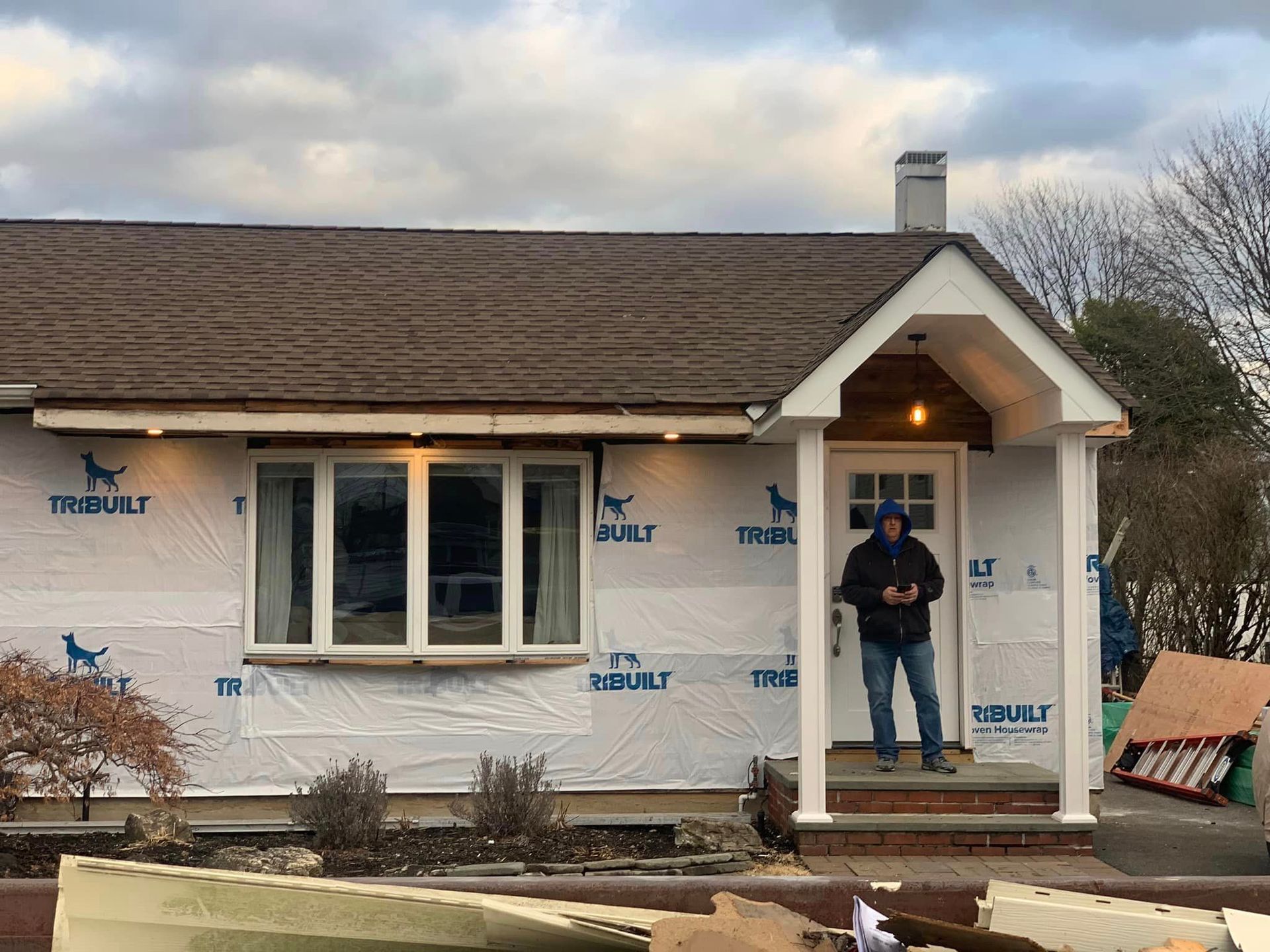 A man is standing on the porch of a house that is being remodeled.