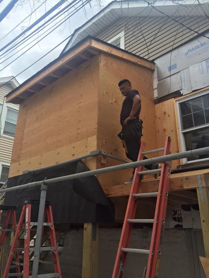 A man is standing on a ladder on the side of a house.