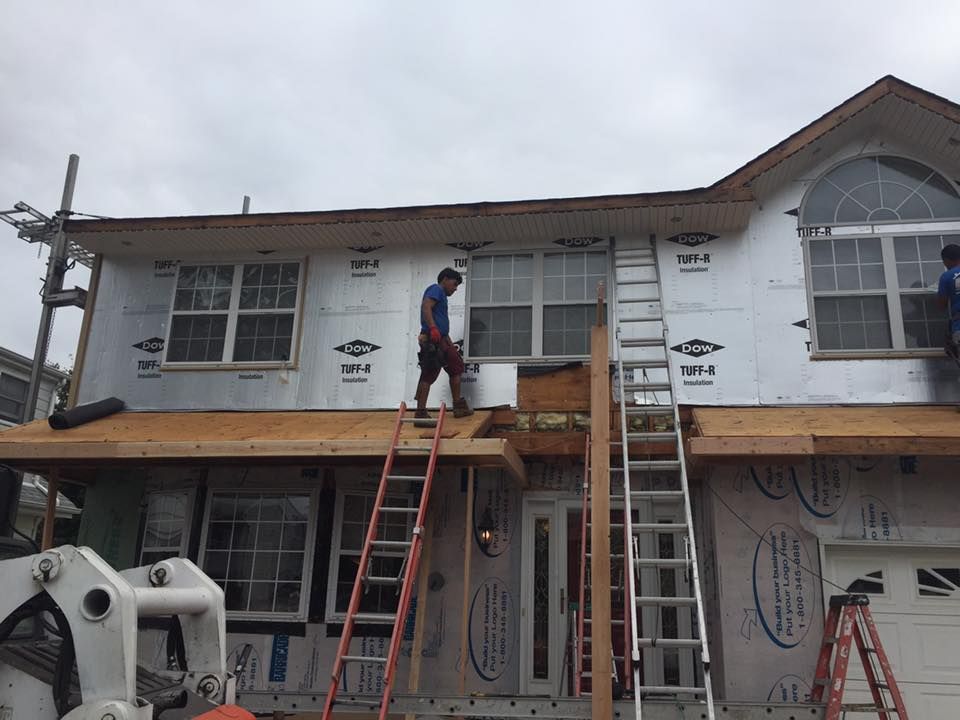 A man is standing on a ladder on the roof of a house.