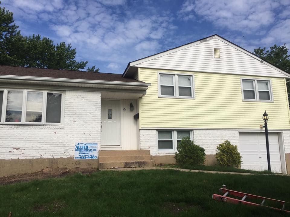 A white house with yellow siding and a ladder in front of it