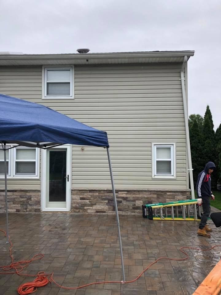 A man is standing in front of a house with a blue tent in front of it.