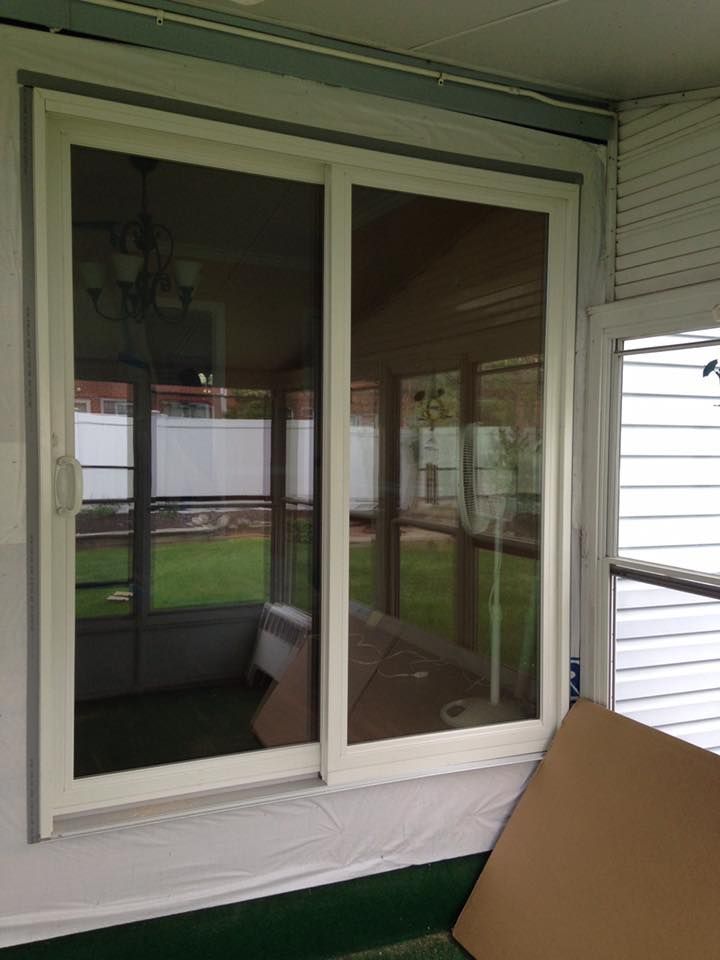 A sliding glass door is sitting on a porch next to a cardboard box.