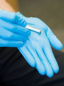 A person wearing blue gloves is holding a dental tool with laser.