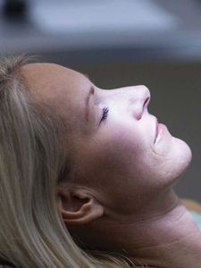 A woman is laying in a dental chair with her eyes closed and smiling.