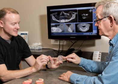 Two men are sitting at a table looking at dentures.