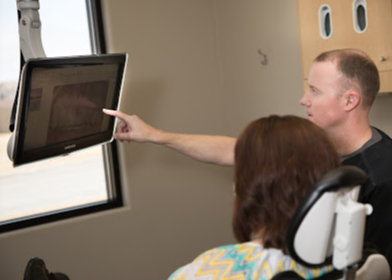 A man is pointing at a screen while a woman sits in a dental chair.