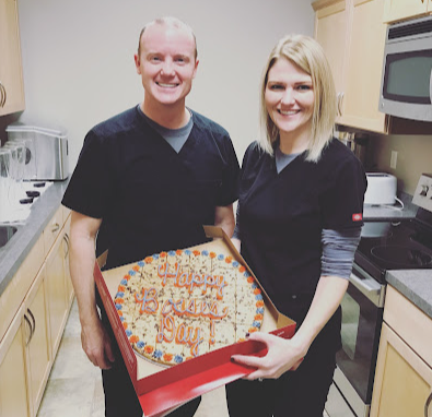 A man and a woman holding a pizza in a kitchen