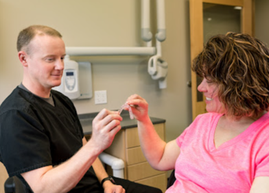 A dentist is talking to a woman in a pink shirt in a dental office.