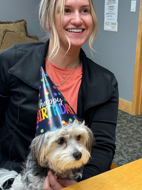A woman is holding a small dog wearing a happy birthday hat
