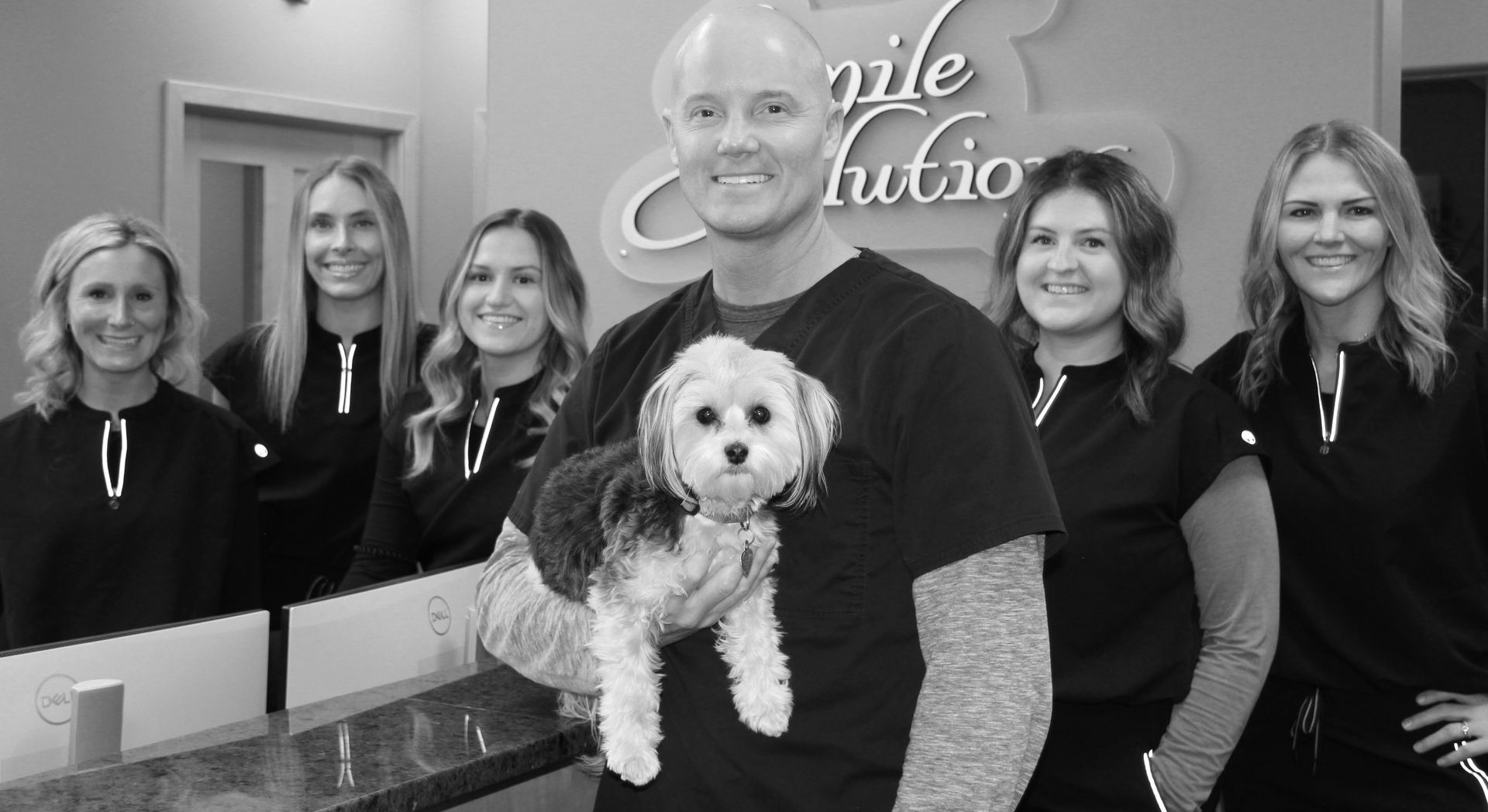 A man is holding a small dog in front of a group of women.