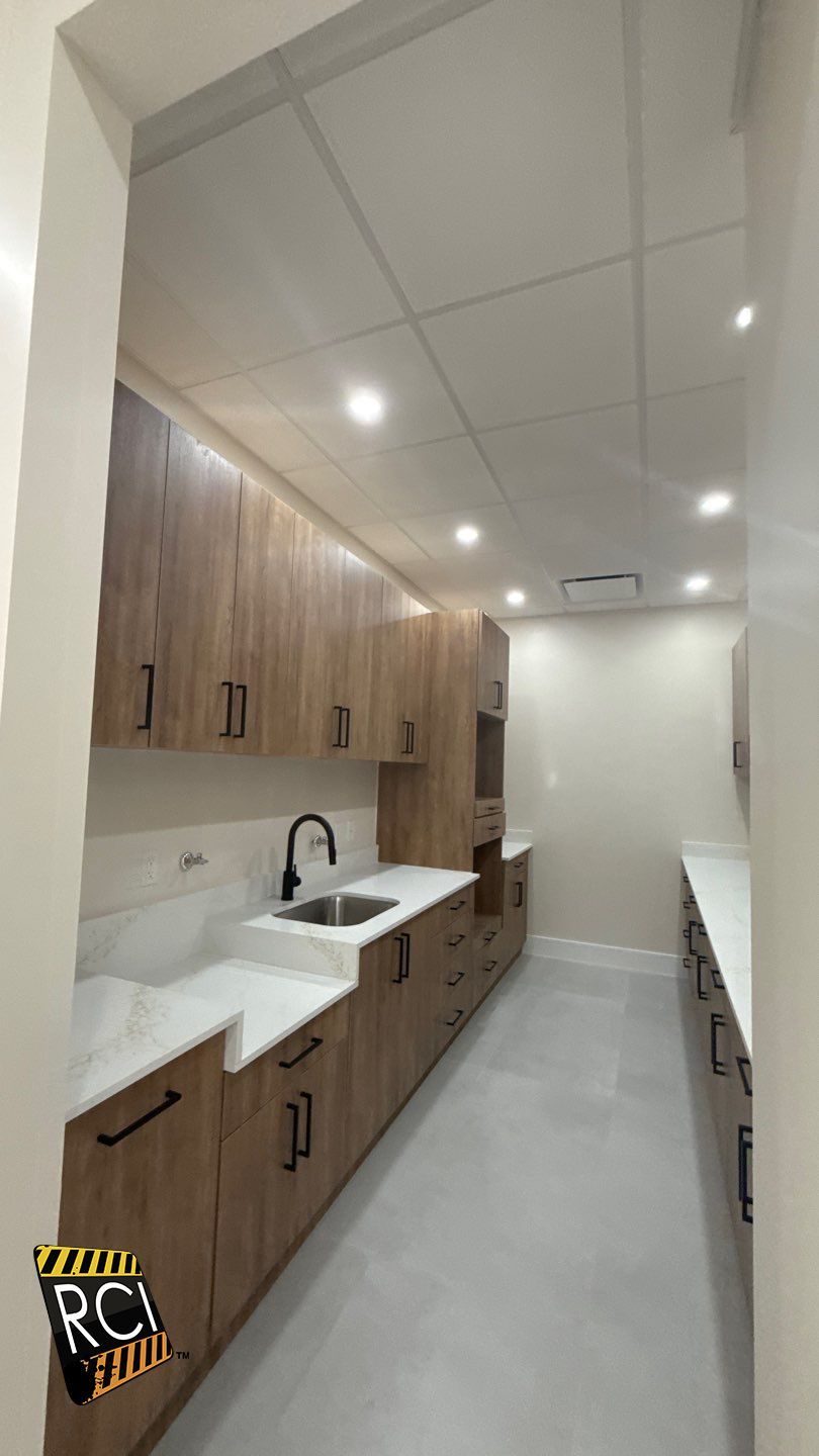 A long kitchen with wooden cabinets and white counter tops.