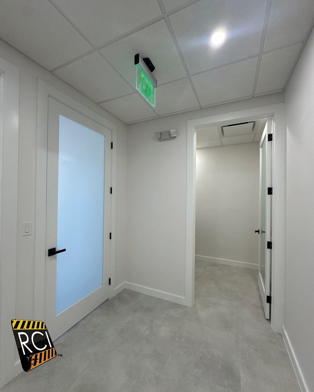 An empty hallway with a green exit sign on the ceiling
