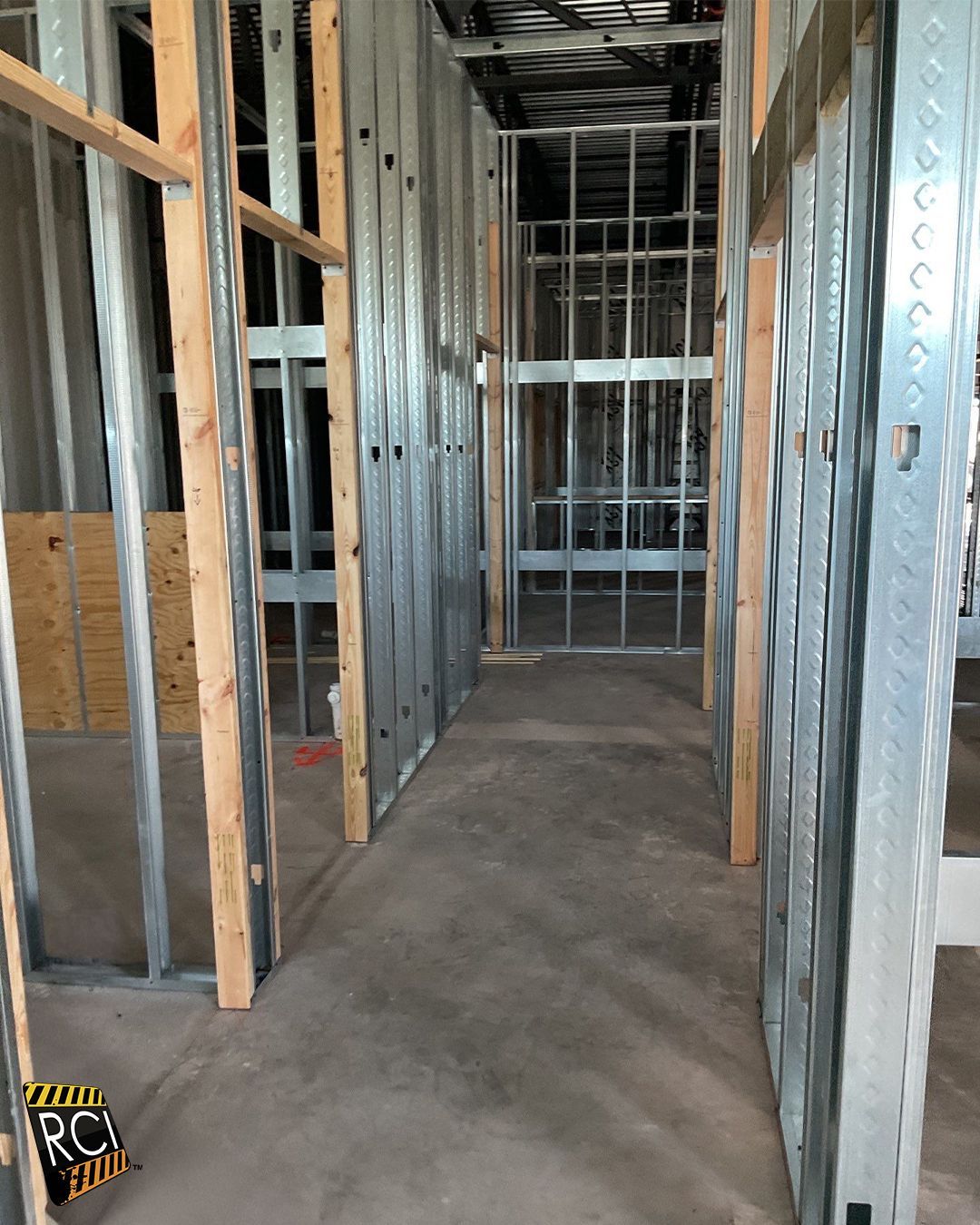 Interior building construction with metal and wood framing in a narrow hallway. Concrete floor.