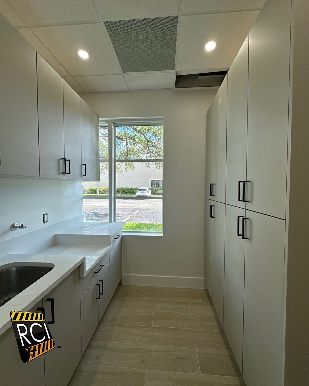 A kitchen with white cabinets , a sink and a window.