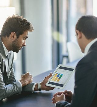 Two men are sitting at a table looking at a tablet.
