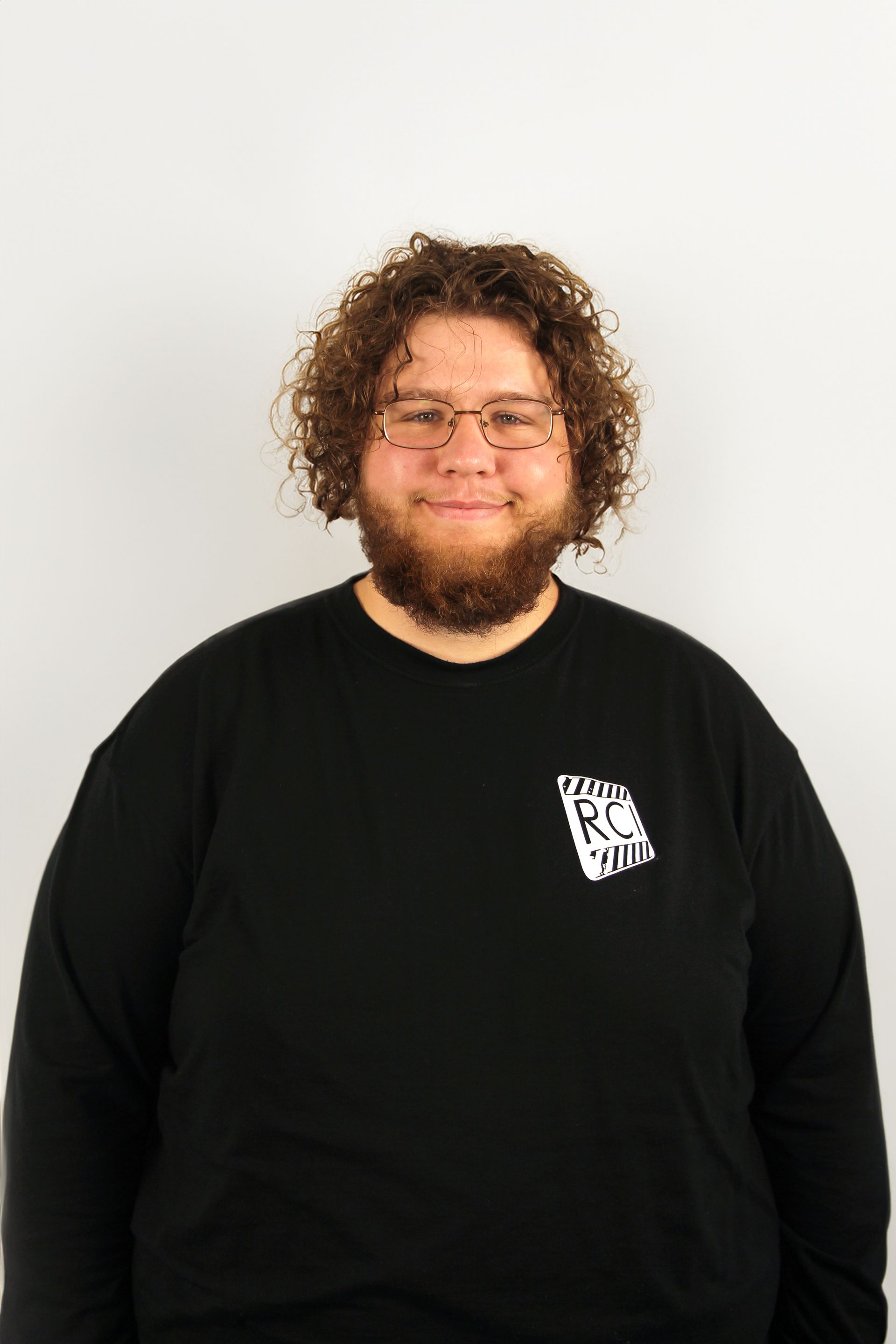 A man with curly hair and a beard is wearing glasses and a black shirt.