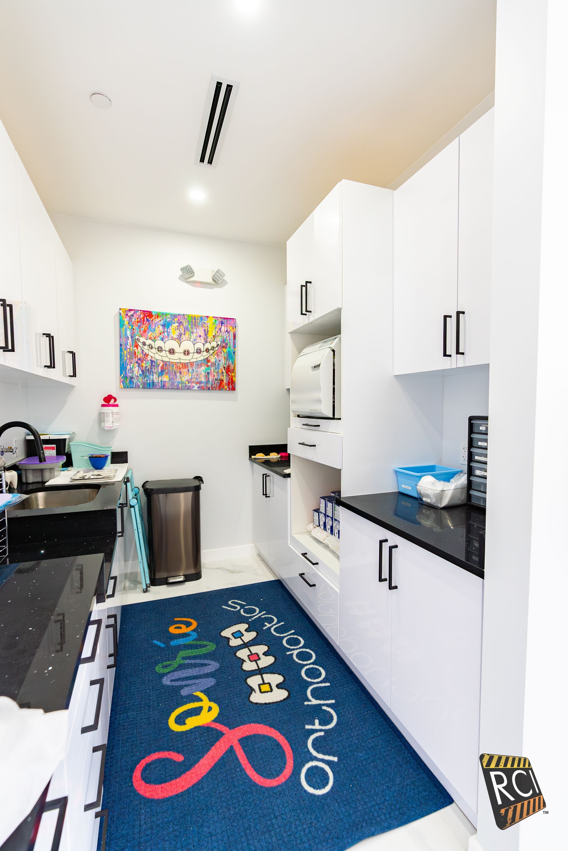 A kitchen with white cabinets and a blue rug that says orthodontics