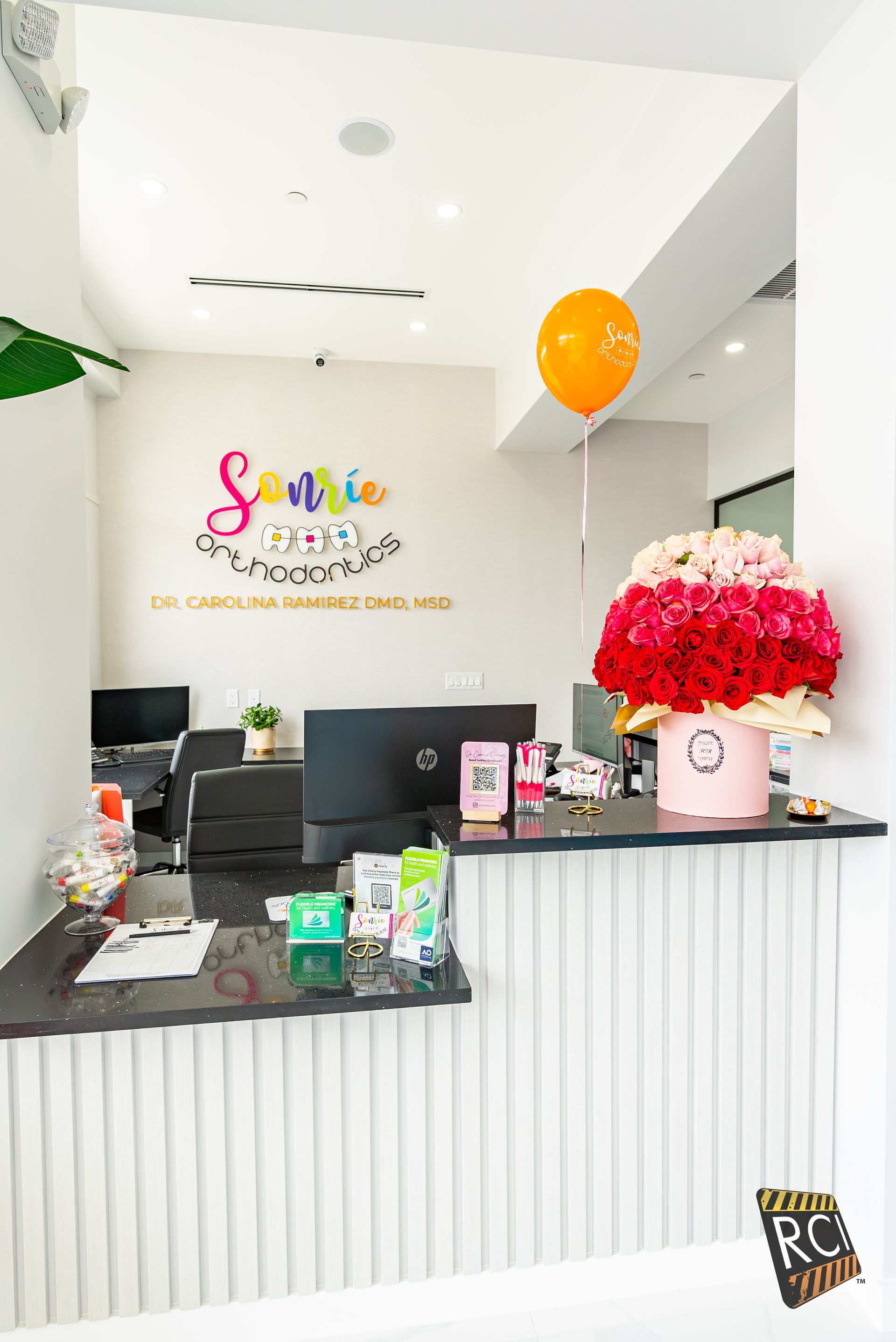 A reception desk with a vase of flowers on it and balloons hanging from the ceiling.