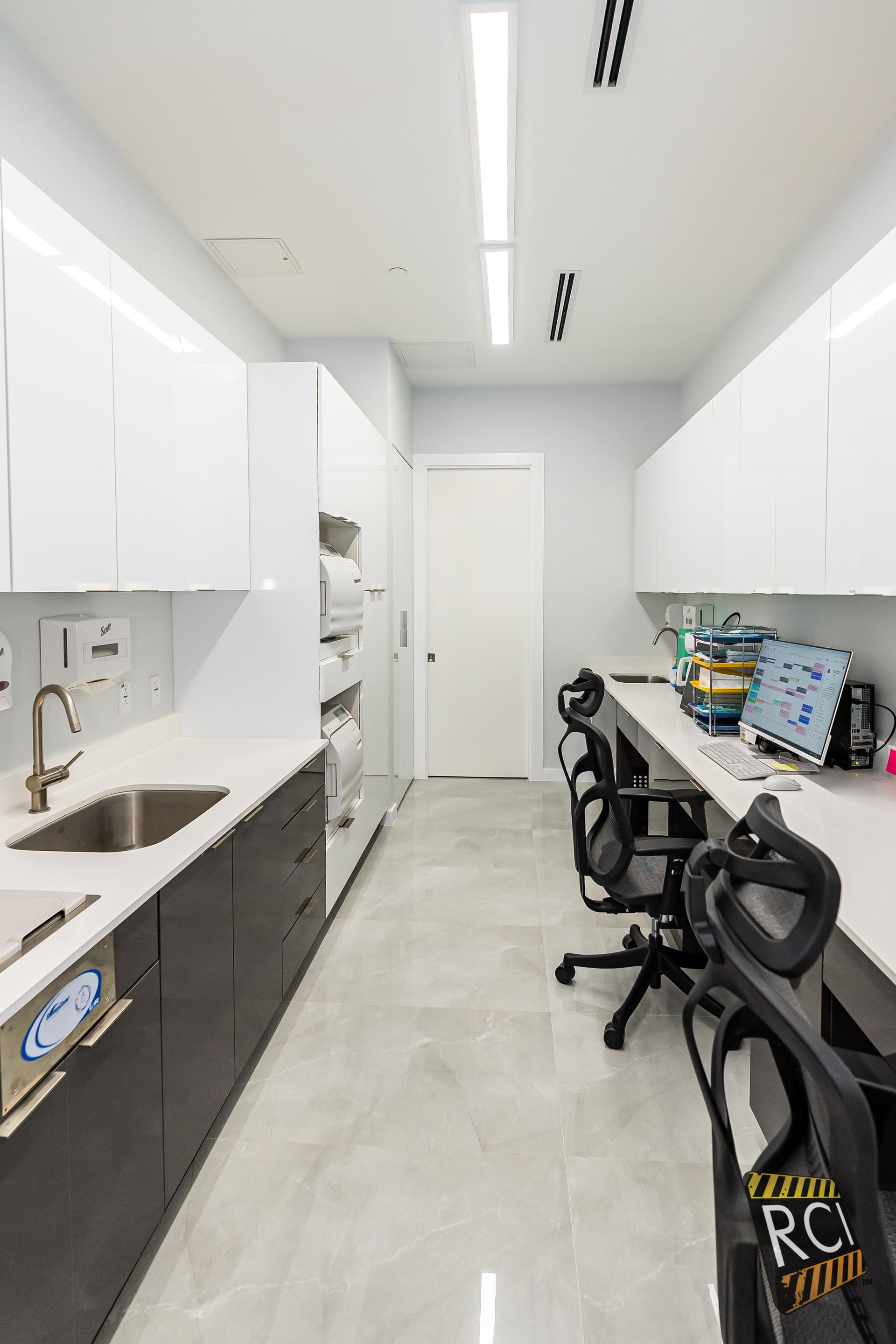 A kitchen with a sink , desks , chairs and cabinets.
