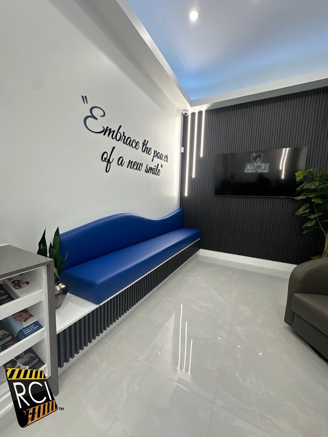 A waiting room with a blue couch and a tv on the wall.