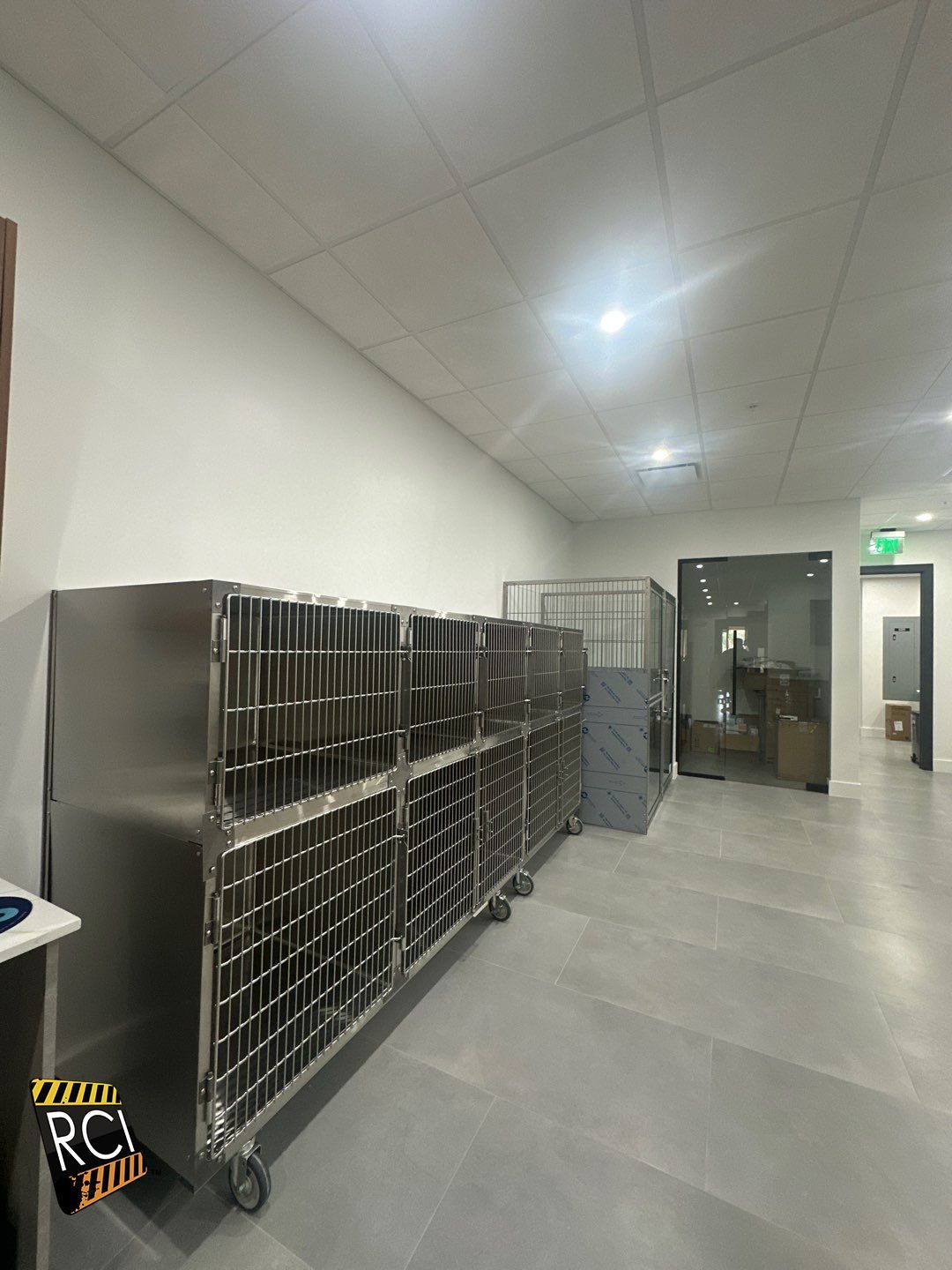 A row of stainless steel cages are lined up in a hallway.