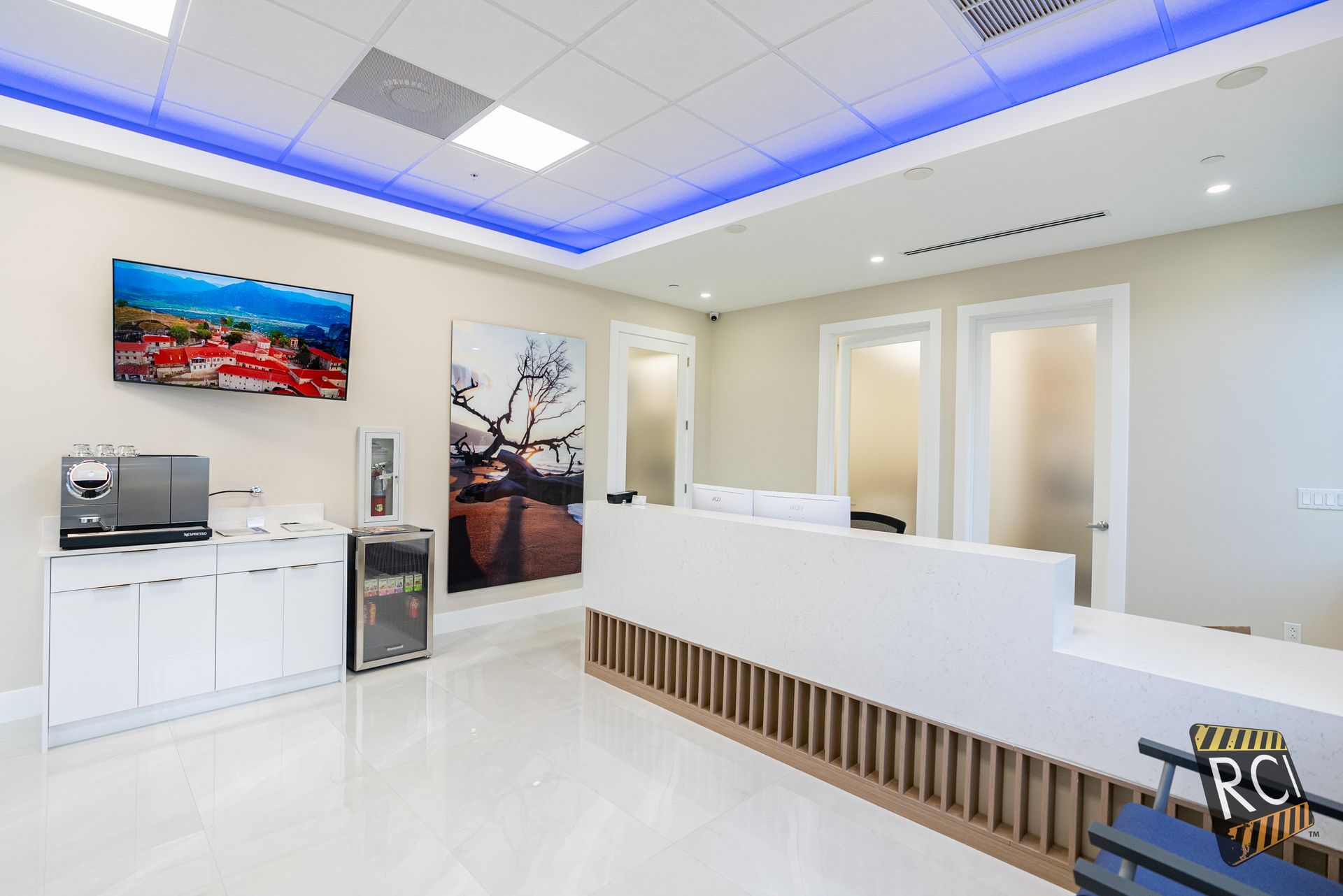 Modern medical office reception area with white counter, art, and coffee station.