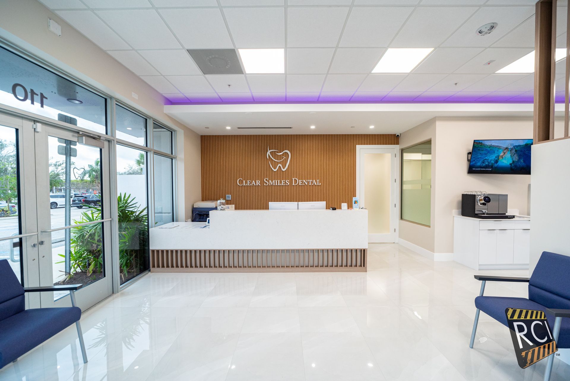 Modern dental office reception area with white desk, wooden accent wall, and blue chairs.