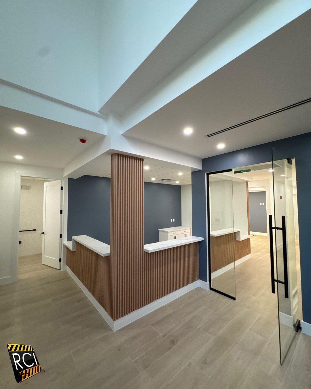 Reception area with light wood and blue walls, glass door, and white countertops.