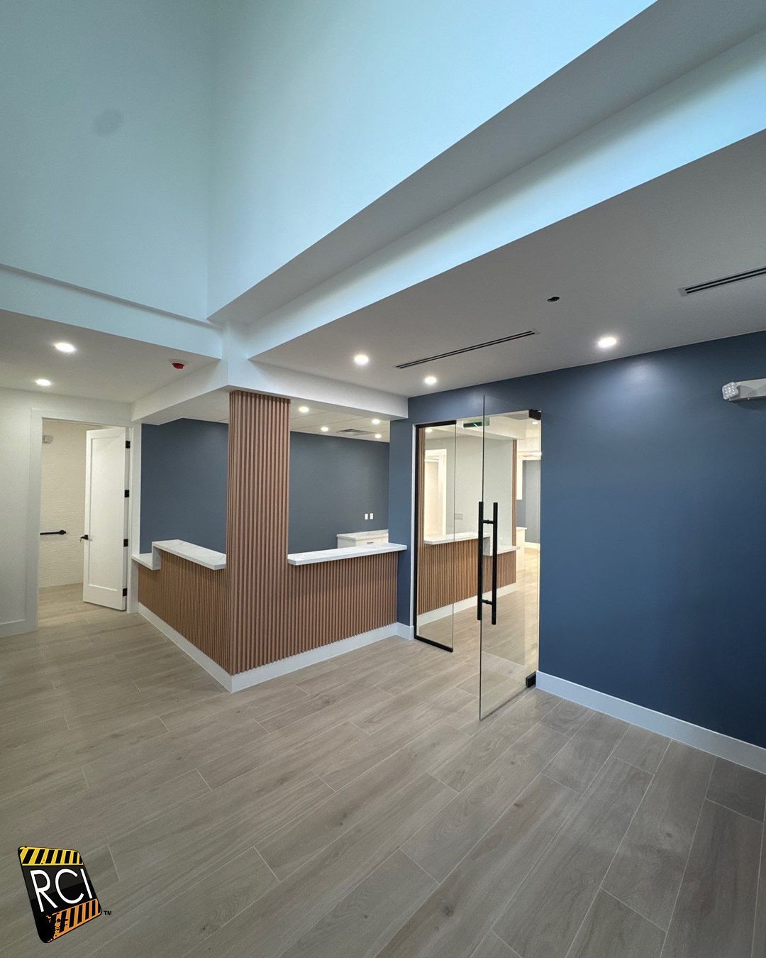 Modern office reception area with blue walls, light wood accents, and glass door.