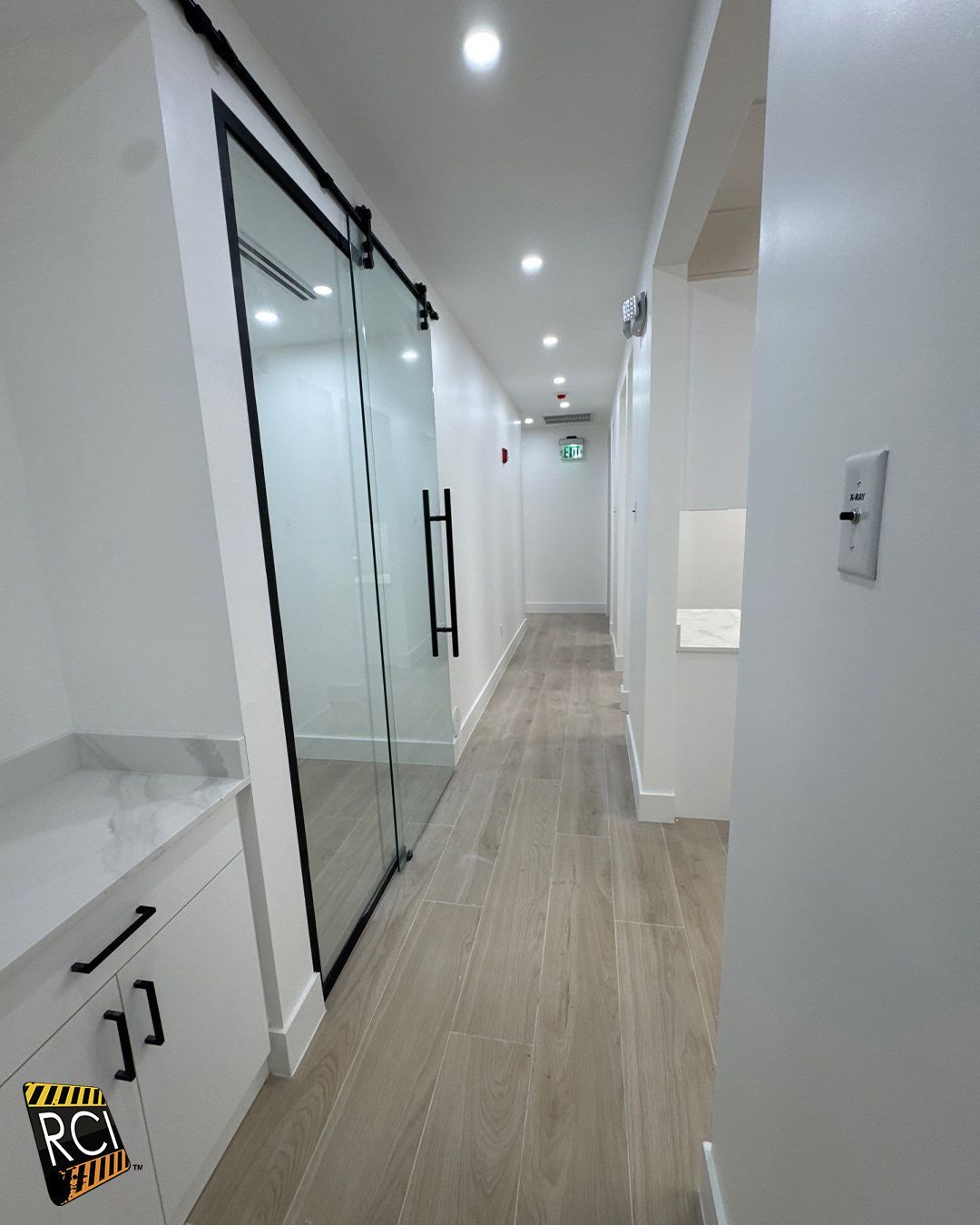 Long, bright hallway with wood-look flooring, glass sliding door, and white walls.