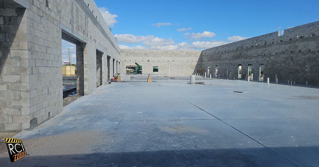 Construction site: unfinished concrete building with open doorways and surrounding walls, blue sky.