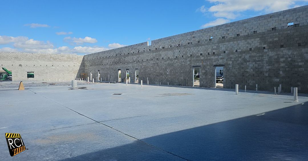 Stone fortress courtyard, blue sky. Long gray walls with rectangular openings.