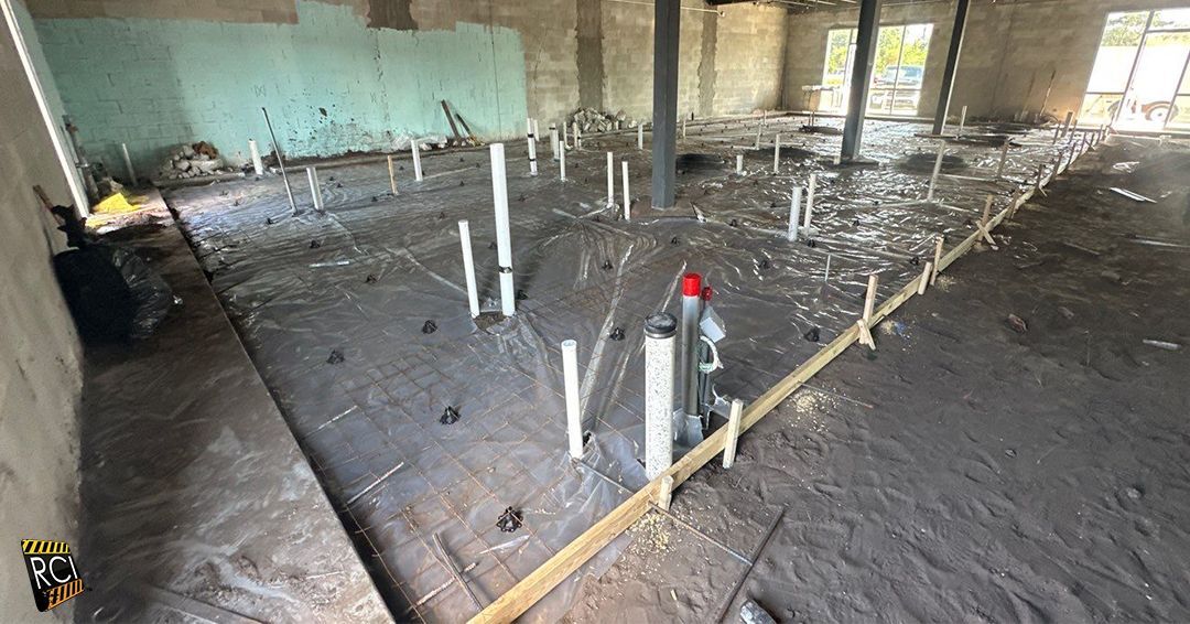 Construction site: concrete floor, plumbing pipes, wooden forms, partially built room.
