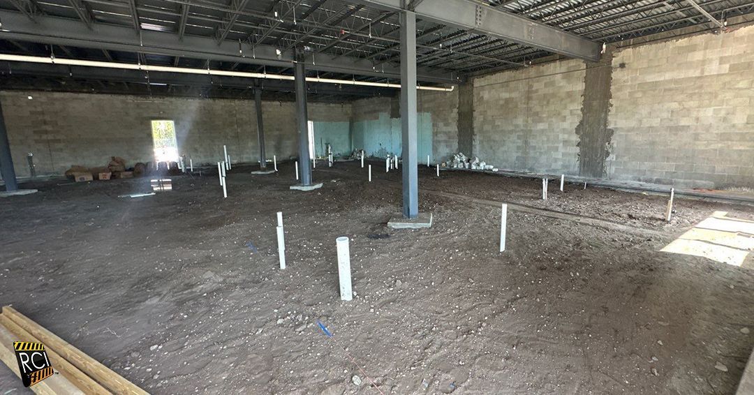 Construction site interior with exposed pipes and dirt floor. Steel beams support the ceiling.