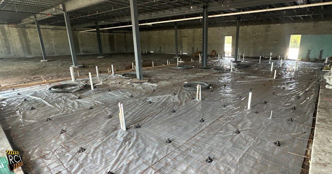 Construction site: Interior of a building with concrete floor, plumbing pipes, and black plastic sheeting.