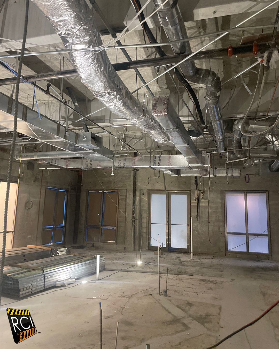 Interior construction site with exposed ductwork, windows, and unfinished walls and floors.