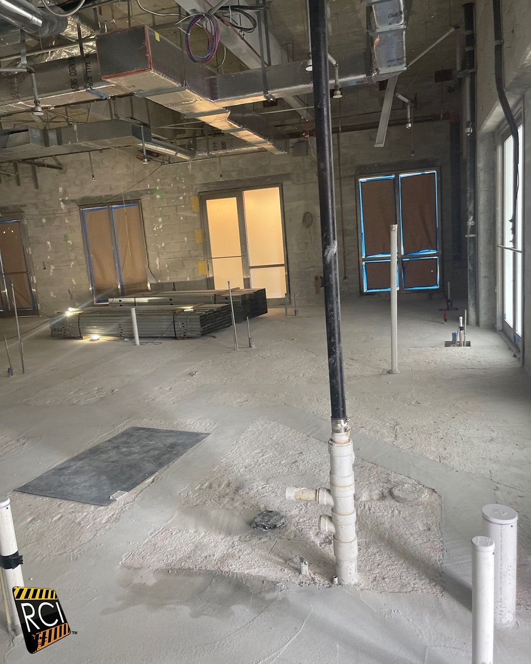 Interior of a building under construction, showing pipes, unfinished walls, and doors.