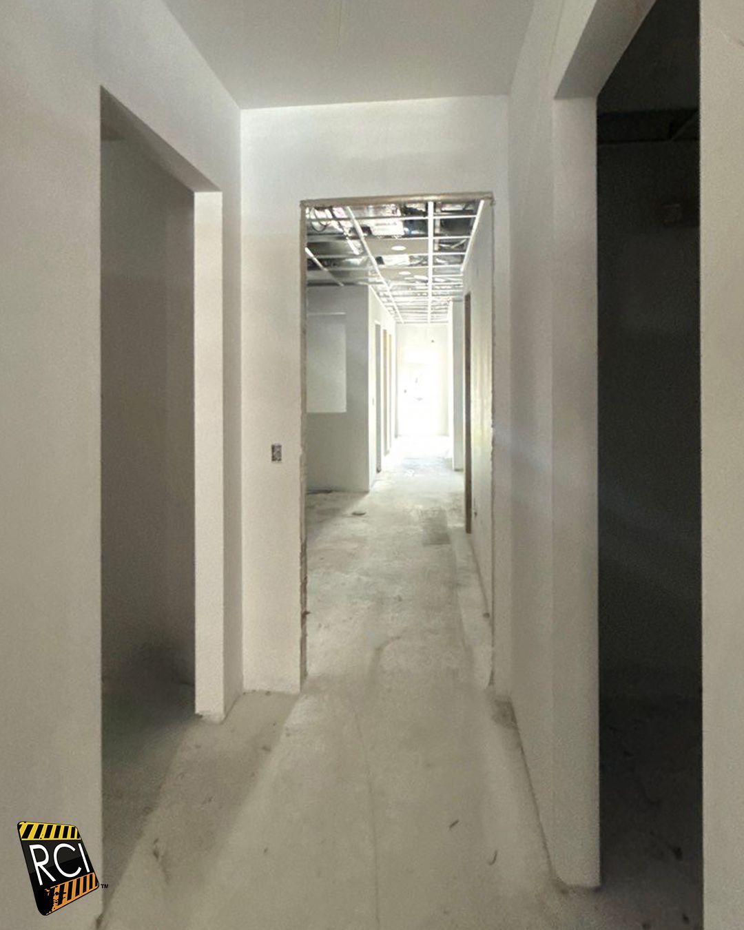 Empty hallway in a building under construction, with open doorways and unfinished ceiling.
